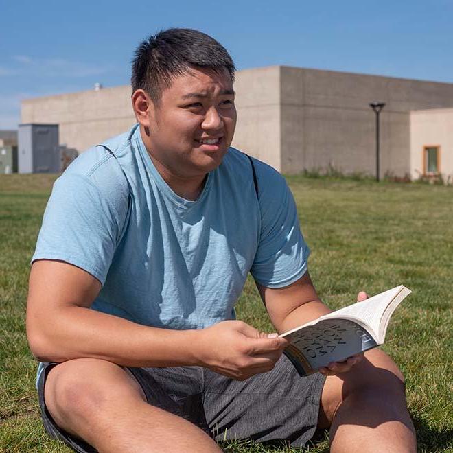 Male year-round campus student studying outside on a summer day